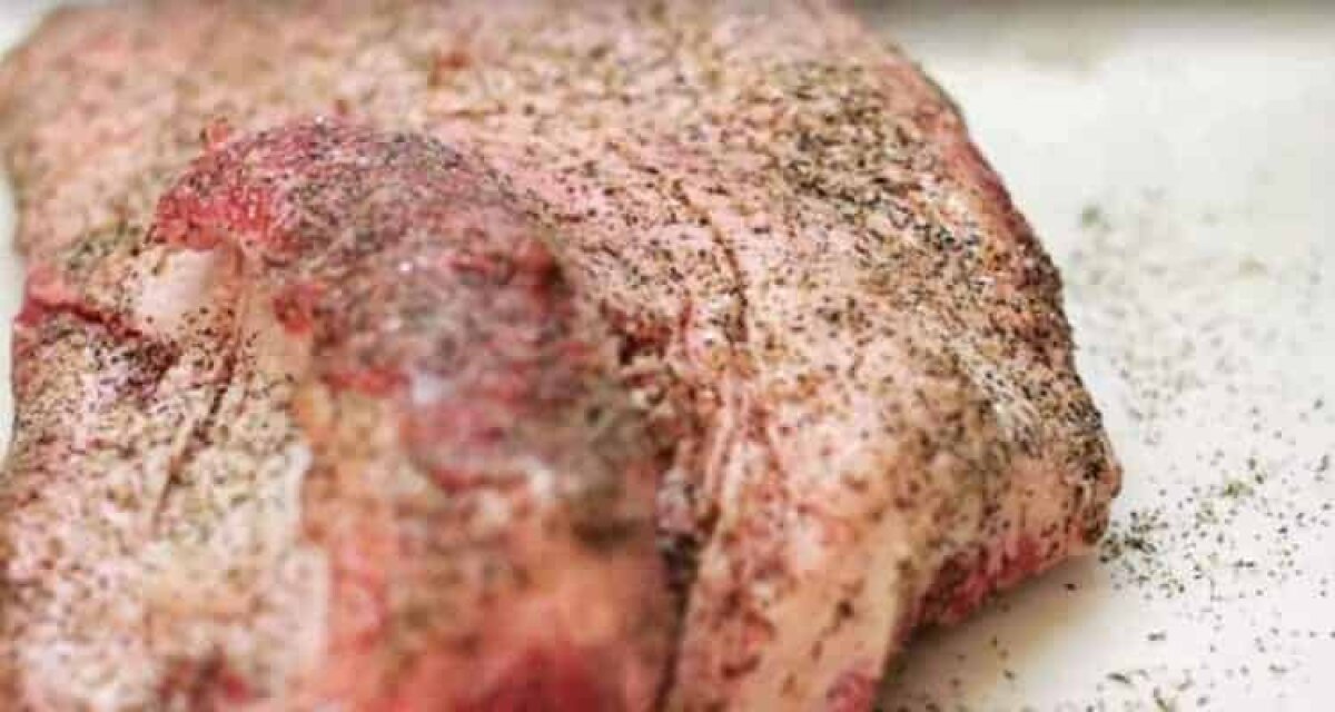 Applying coarse salt and black pepper Dalmatian rub to seasoned Texas brisket