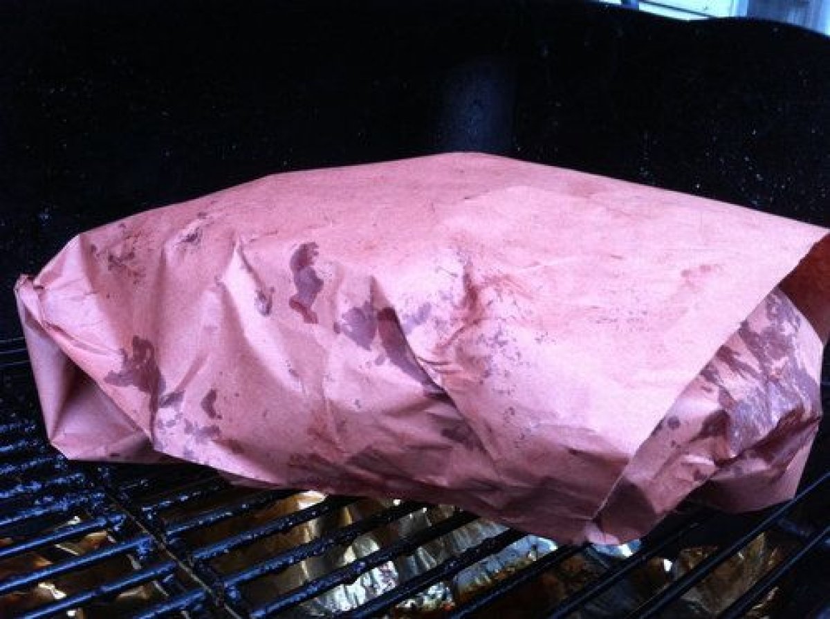 Wrapping smoked brisket tightly in peach butcher paper to preserve bark and retain moisture