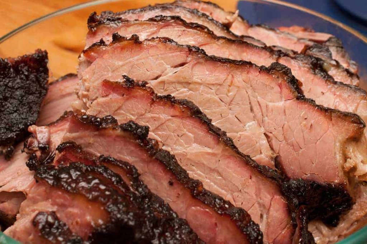 Slicing tender smoked Texas brisket against the grain with visible smoke ring and bark